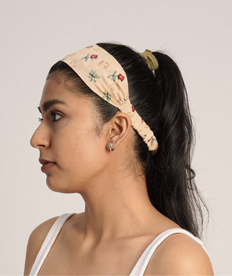 Woman wearing a beige elastic headband with small floral prints, side view, paired with a green scrunchie in a ponytail