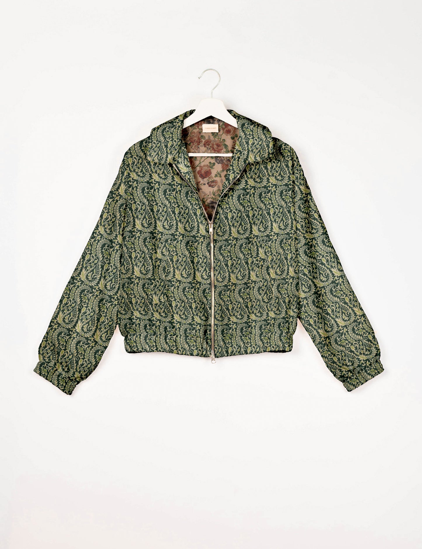 Green bomber jacket with cream leaf pattern, front zipper, elastic cuffs, and floral inner lining, hanging on white hanger