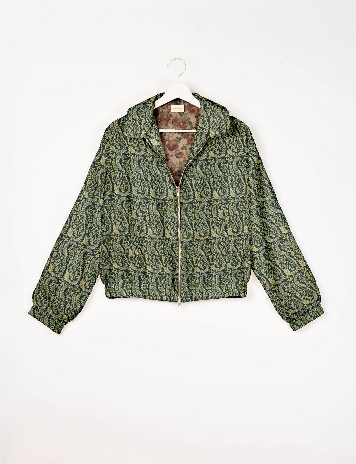 Green bomber jacket with cream leaf pattern, front zipper, elastic cuffs, and floral inner lining, hanging on white hanger