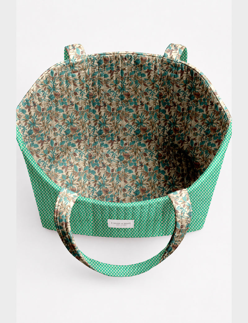 Quilted beach bag with yellow tropical exterior and red patterned interior, shown from top view with handles visible