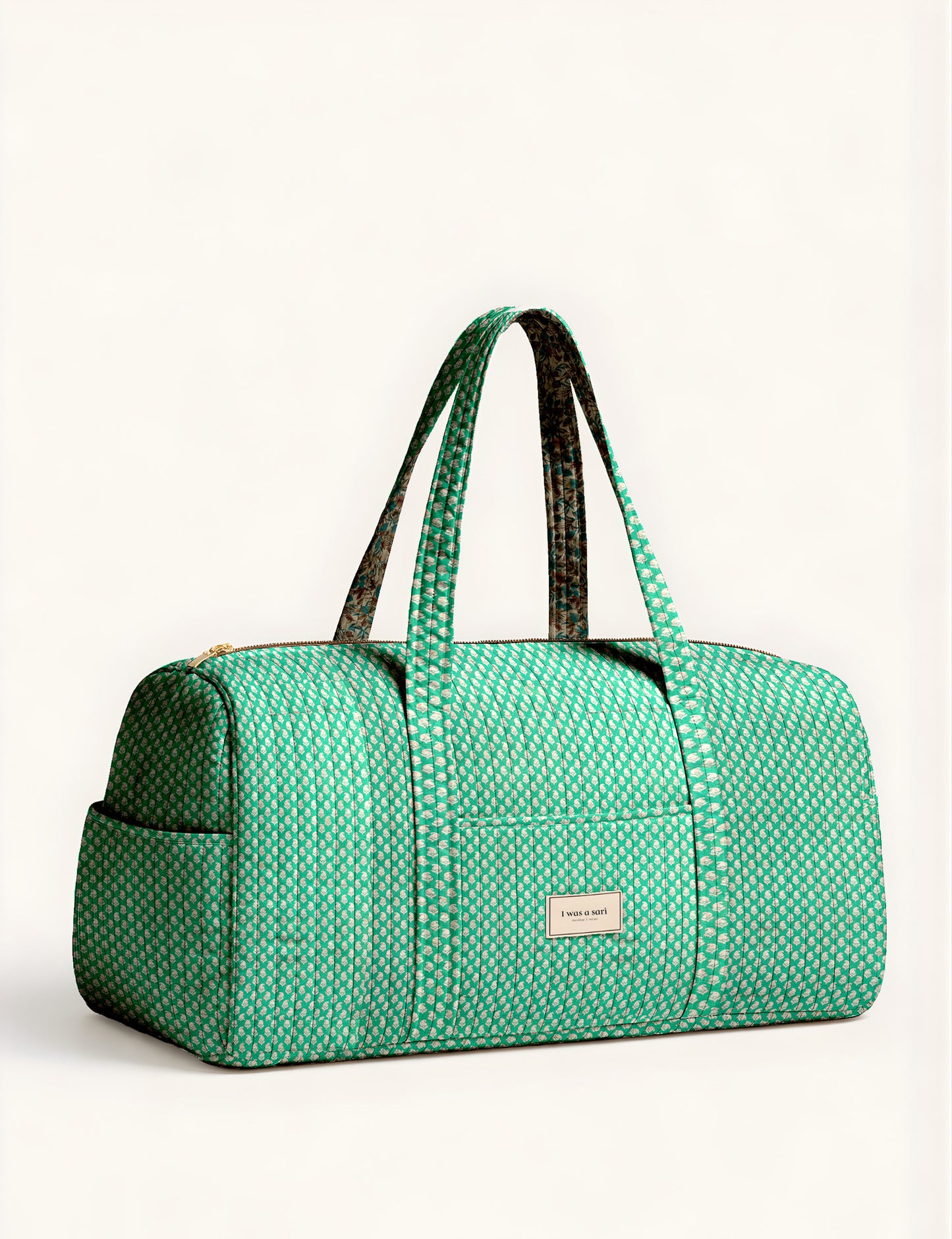 Quilted brown paisley barrel bag with double handles, front pocket, and gold zipper, shown in side angle view