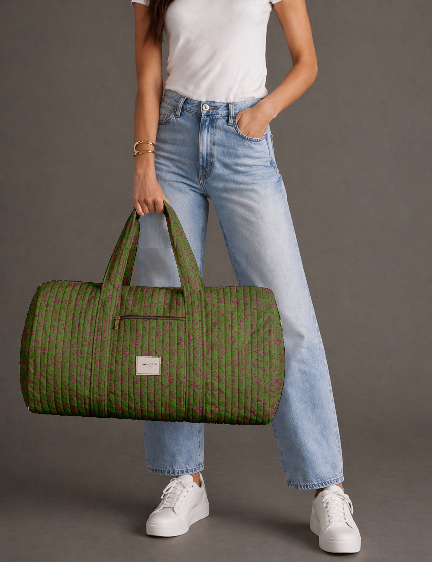 Woman holding a brown paisley quilted barrel bag with front zipper pocket, wearing light blue jeans and white sneakers