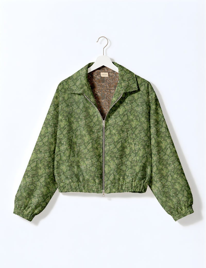 Green bomber jacket with tropical floral and paisley print, front zipper, elastic cuffs, and collar, hanging on white hanger
