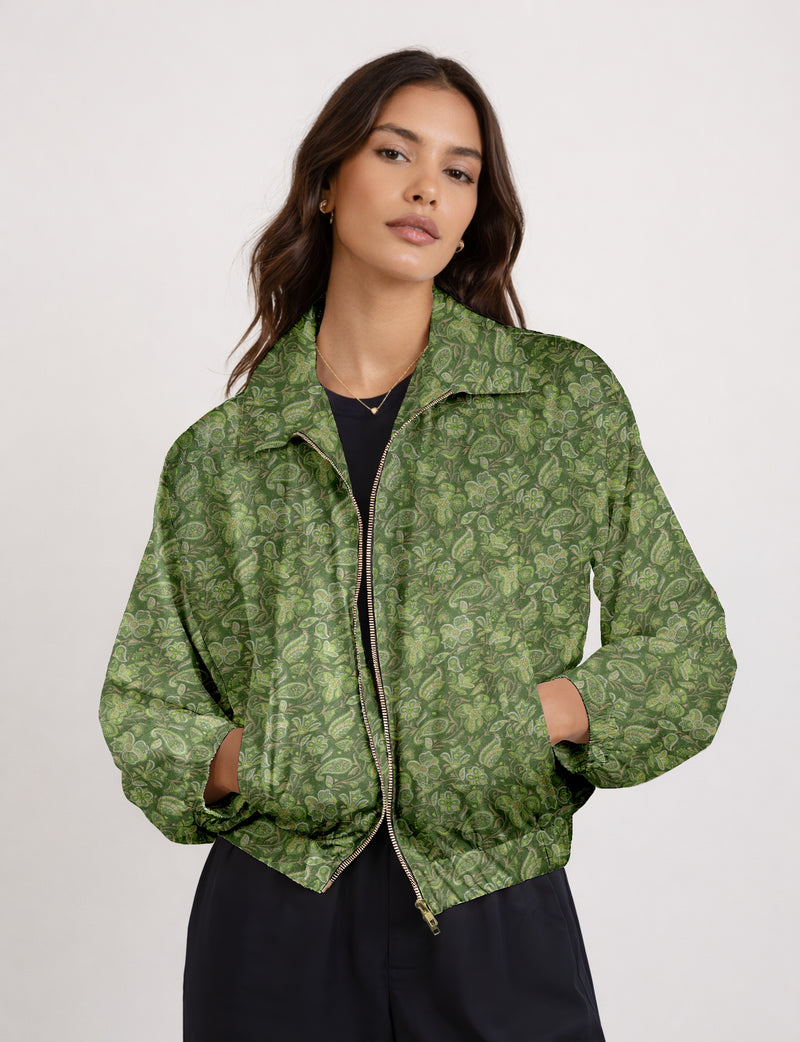 Woman wearing green tropical print bomber jacket with front zipper, elastic cuffs, and side pockets, shown from front waist up