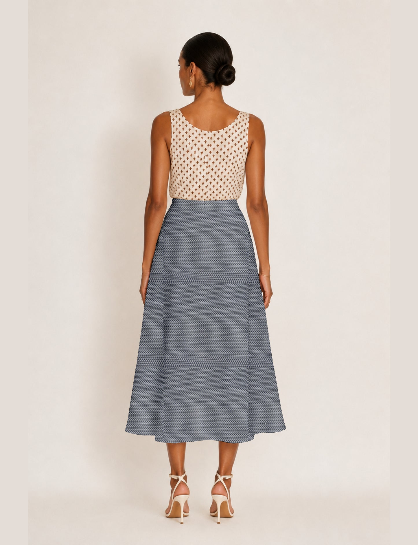 Woman wearing a yellow micro design A-line skirt with side slit, paired with a sleeveless beige top with small cross