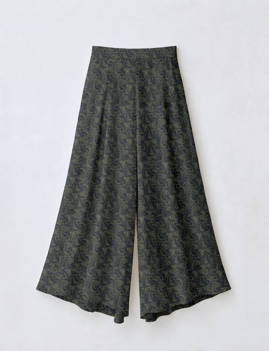 Woman wearing blue wide leg palazzo trousers with black and brown tropical floral print, side pockets, shown from back angle