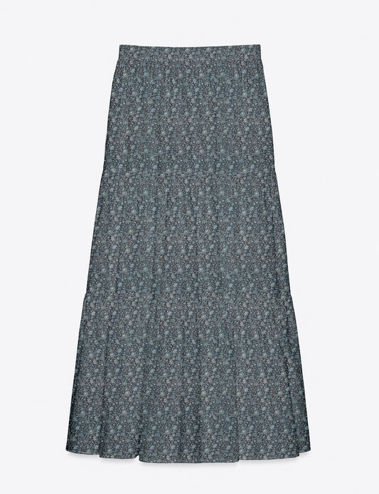 Woman wearing a yellow midi tiered skirt with a small geometric pattern, paired with a beige strapless top and white heels