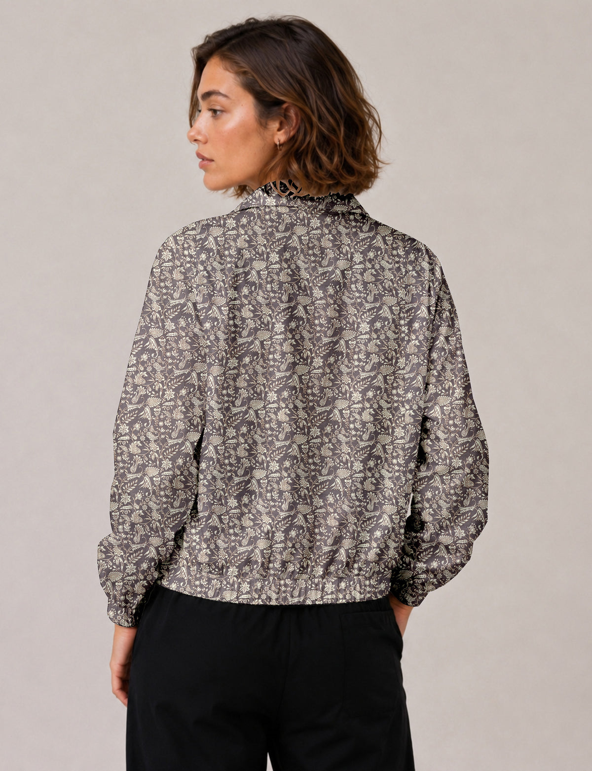 Brown floral bomber jacket with front zipper, elastic cuffs and hem, hanging on white hanger, red floral inner lining visible