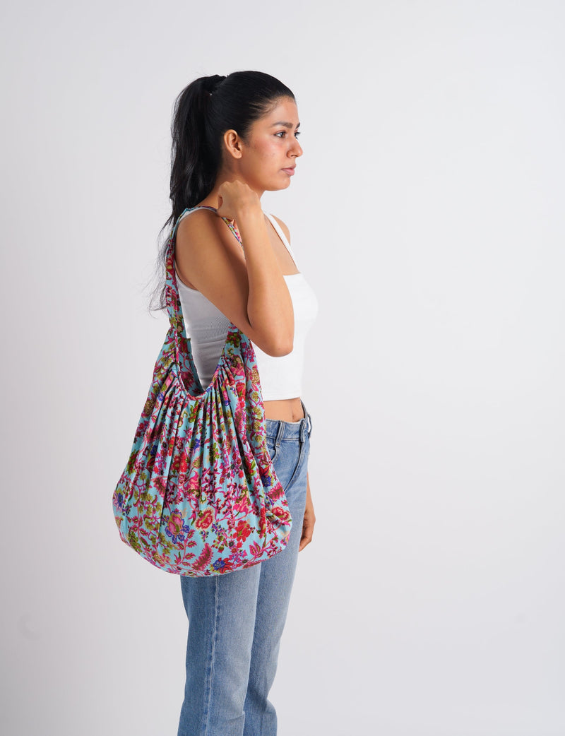 Woman wearing a blue hobo bag with pink and green floral tropical print over her shoulder, side view, white tank top and jeans