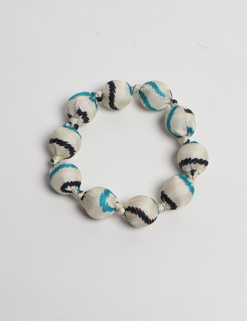 White fabric beaded bracelet with black and teal tropical pattern, knotted between each bead, flat lay on white background