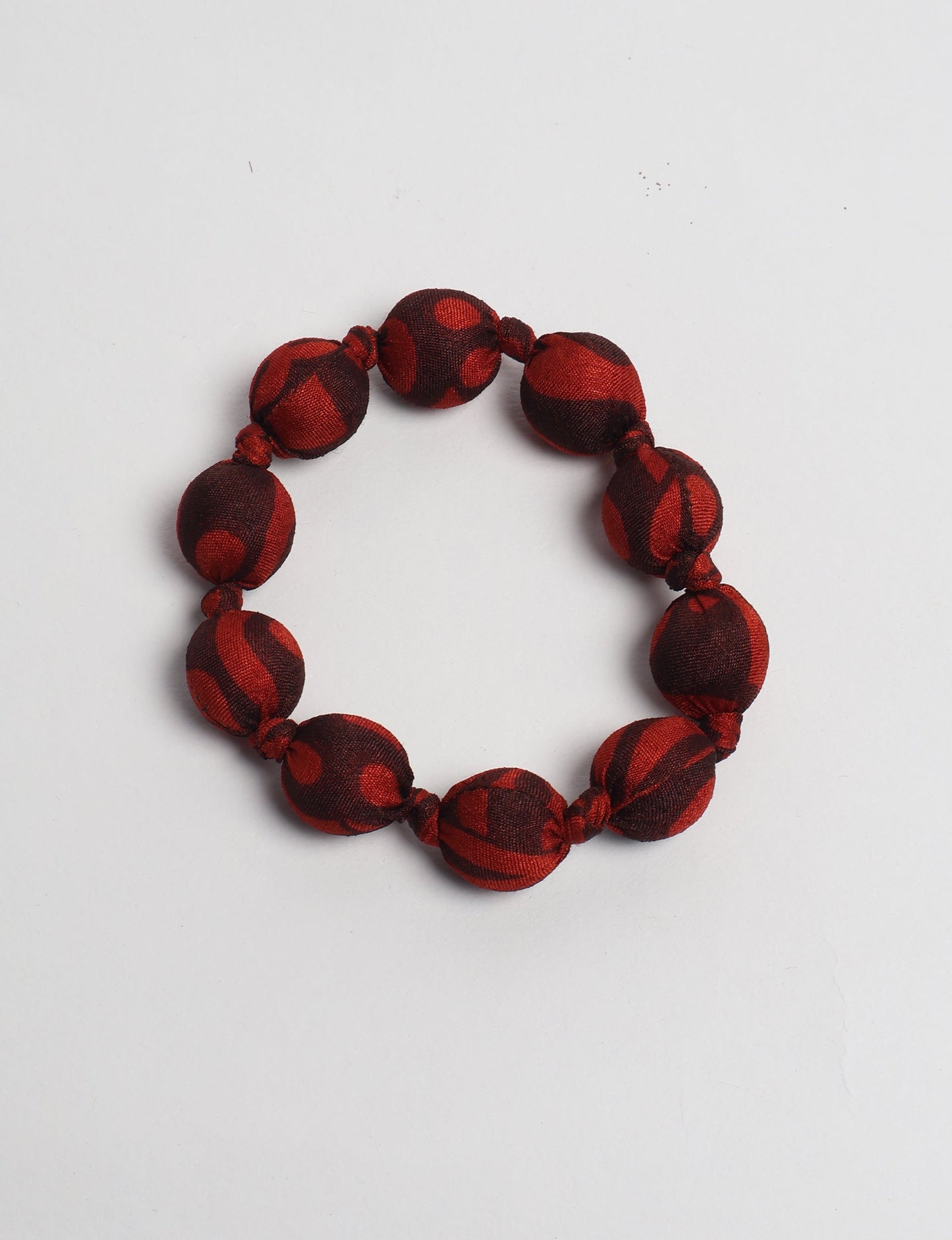 Red and dark brown fabric beaded bracelet with knotted details, flat lay on white background