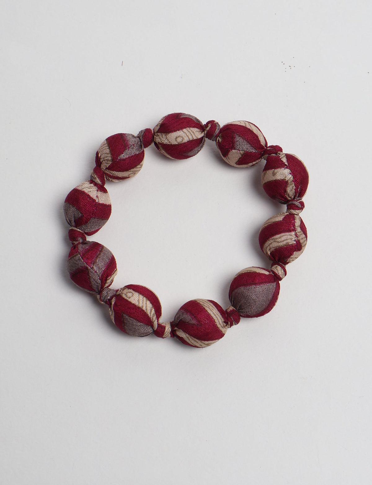 Red and beige striped fabric beaded bracelet with knotted details, shown flat on a white background