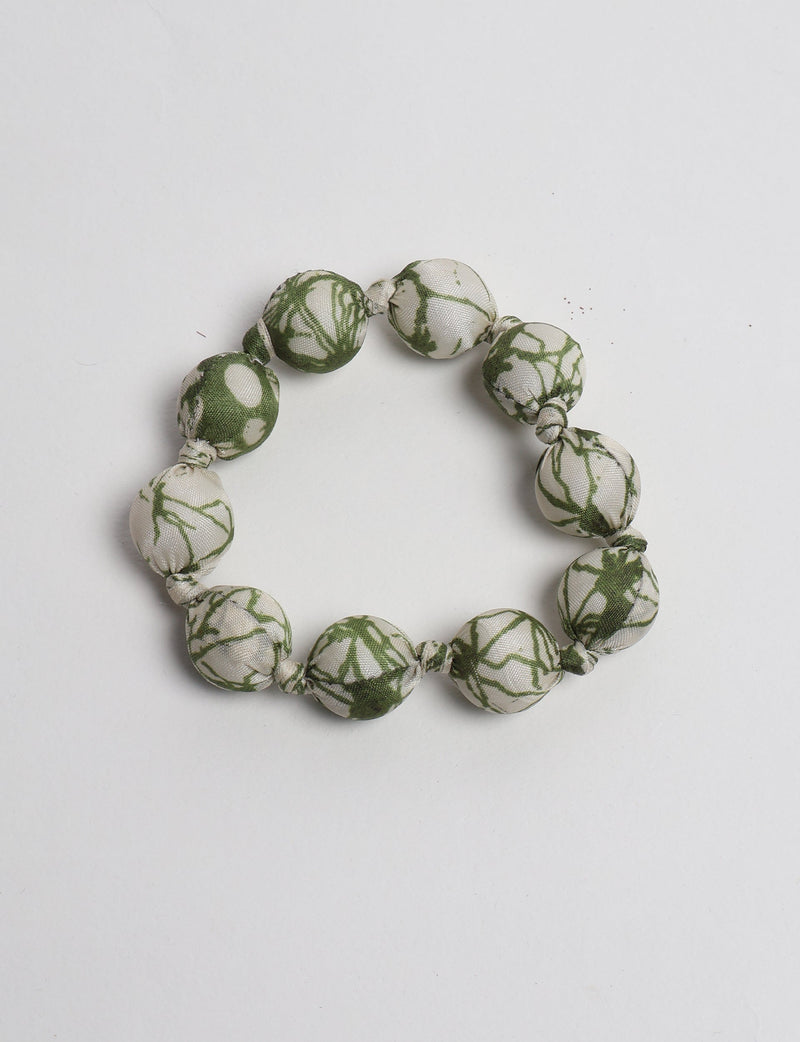 Beaded knotted bracelet with beige and green tropical patterned fabric-covered round beads, flat lay on white background