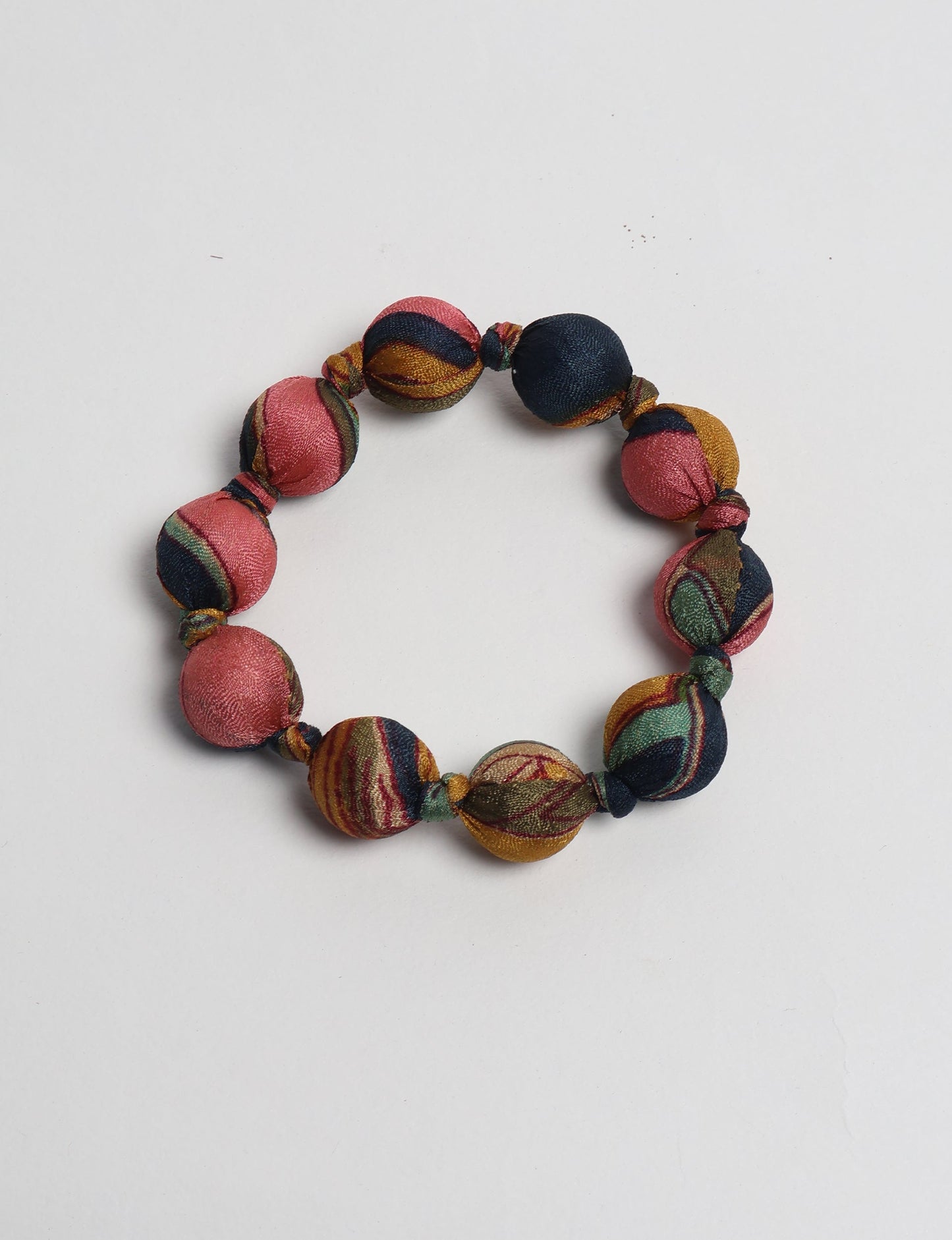 Knotted bracelet with round fabric beads in pink, navy, mustard, and green tropical pattern, flat lay on white background