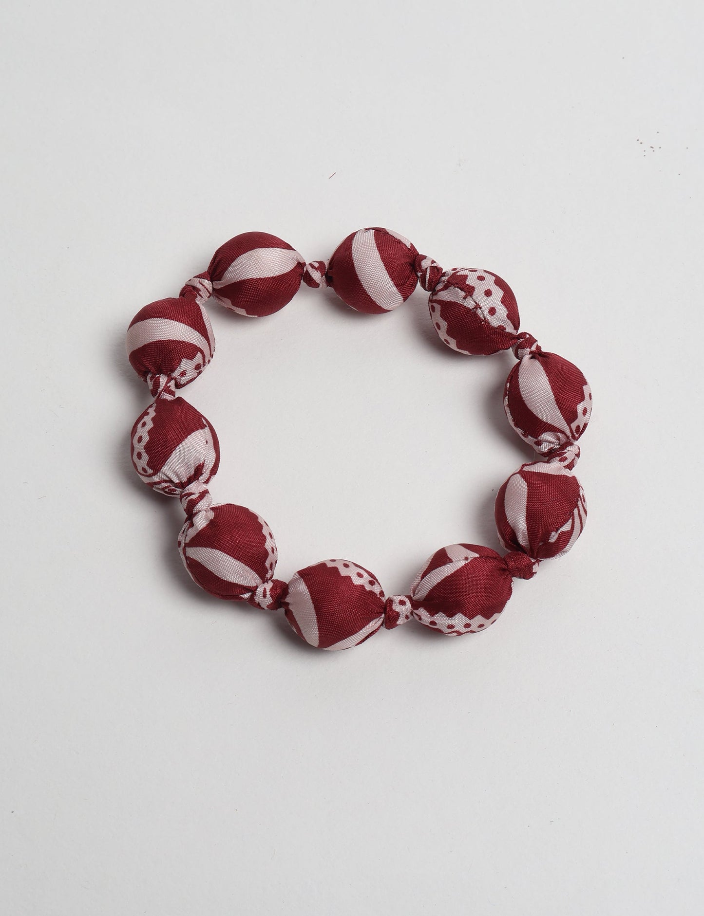 Red and white patterned fabric beaded bracelet with knotted details, shown flat on a white background