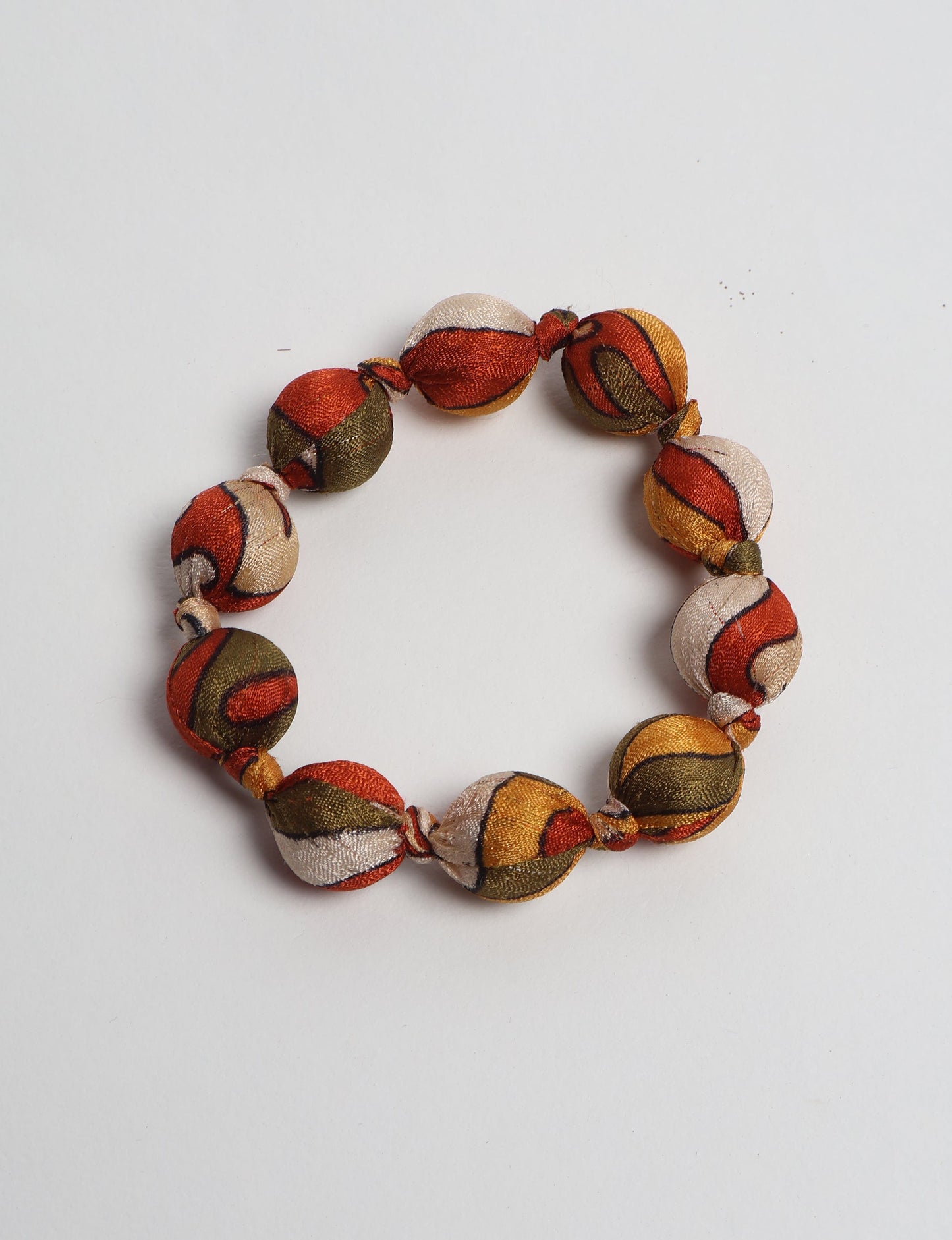 Knotted bracelet with round fabric beads in orange, green, yellow, and cream tropical pattern, flat lay on white background