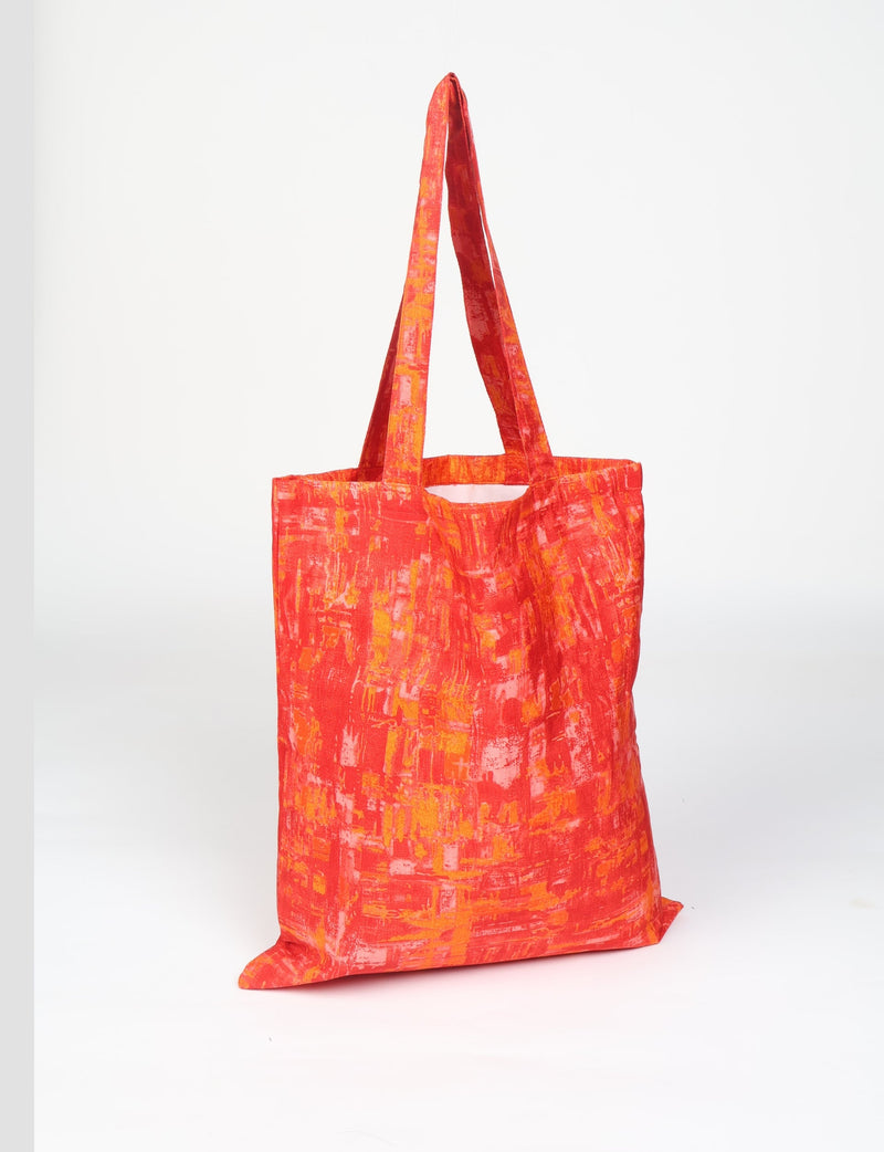 Orange abstract patterned fabric shopper bag with long handles, shown hanging against a white background
