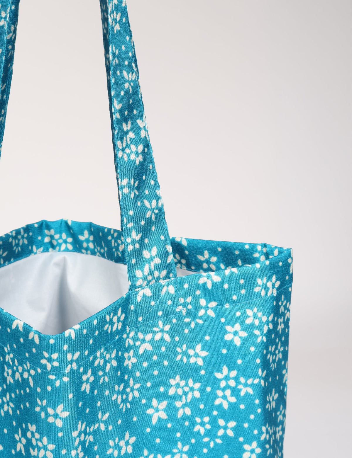 Blue floral patterned fabric shopper bag with matching handles, shown in close-up front view with white interior lining visible