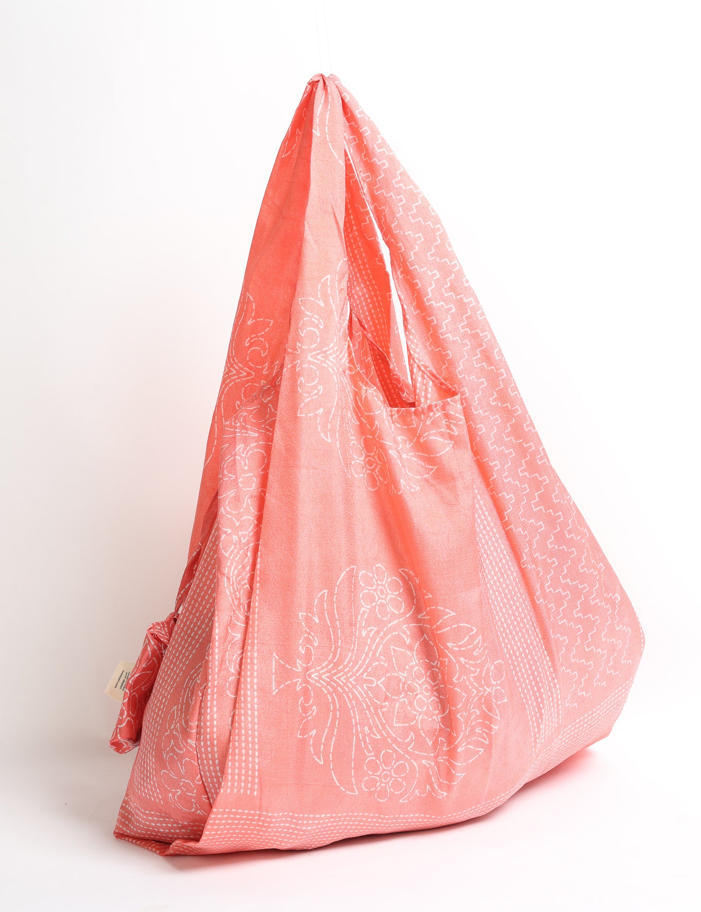 Pink reusable bag with white floral and geometric patterns, hanging by its handles against a white background