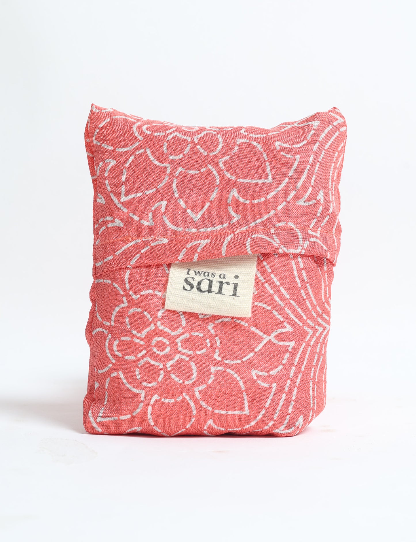 Pink reusable bag with white floral pattern folded, featuring a label that reads "I was a sari" on front
