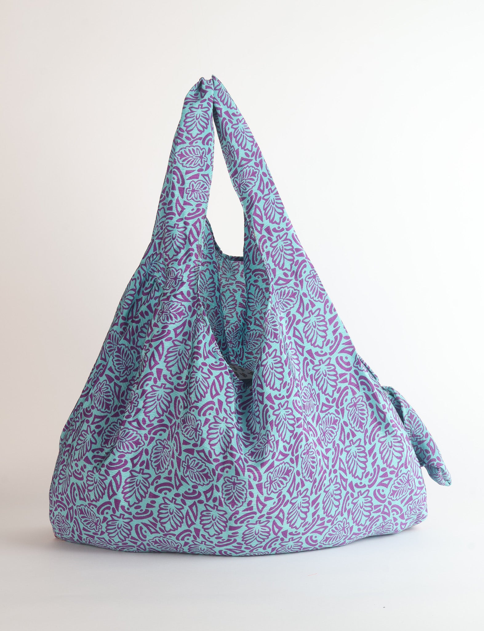 Blue reusable fabric bag with purple leaf pattern, shown hanging with handles visible against white background