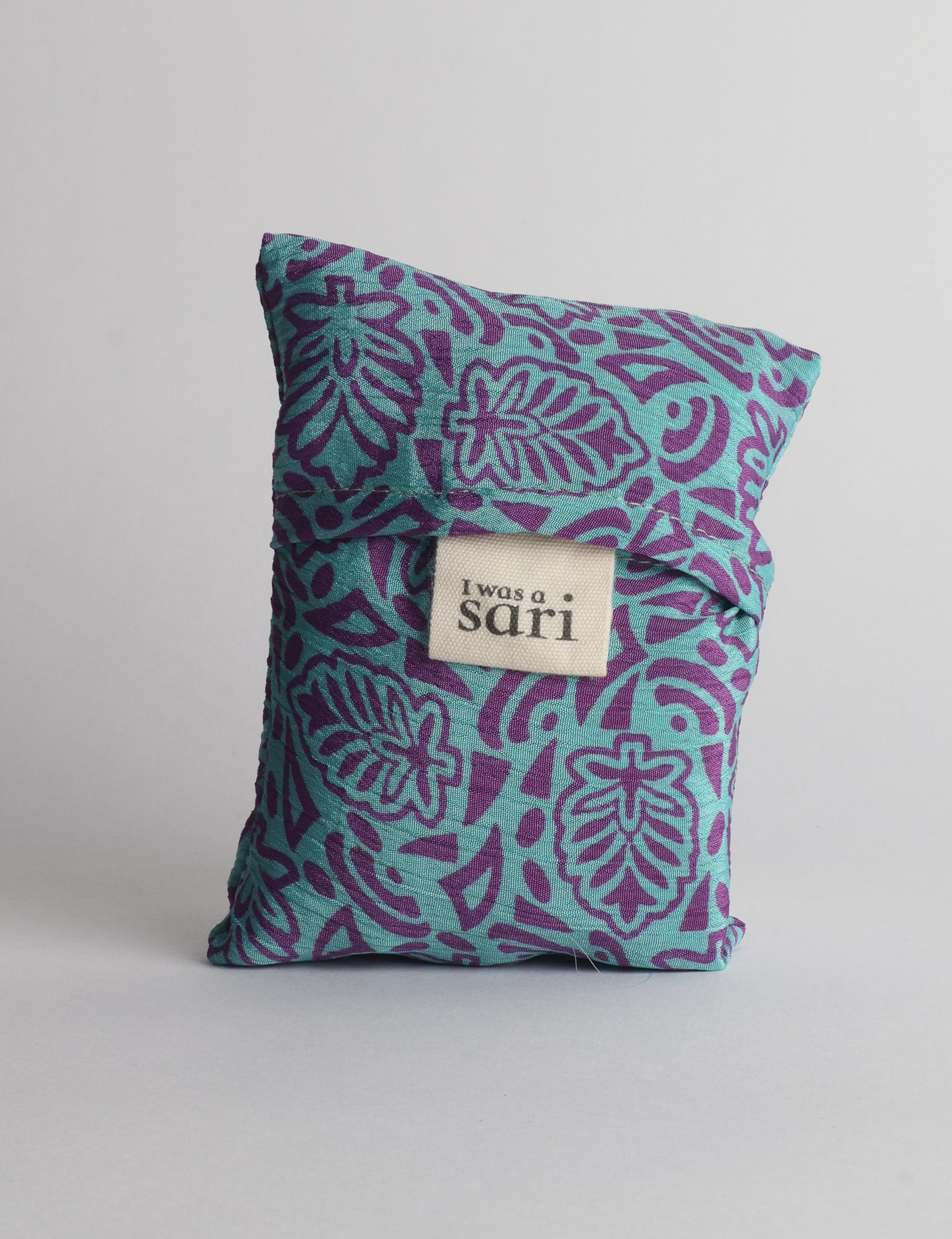 Reusable bag folded with blue fabric featuring purple leaf patterns and a white label reading "I was a sari"