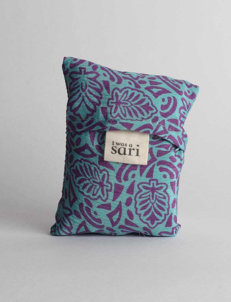 Reusable bag folded with blue fabric featuring purple leaf patterns and a white label reading "I was a sari"