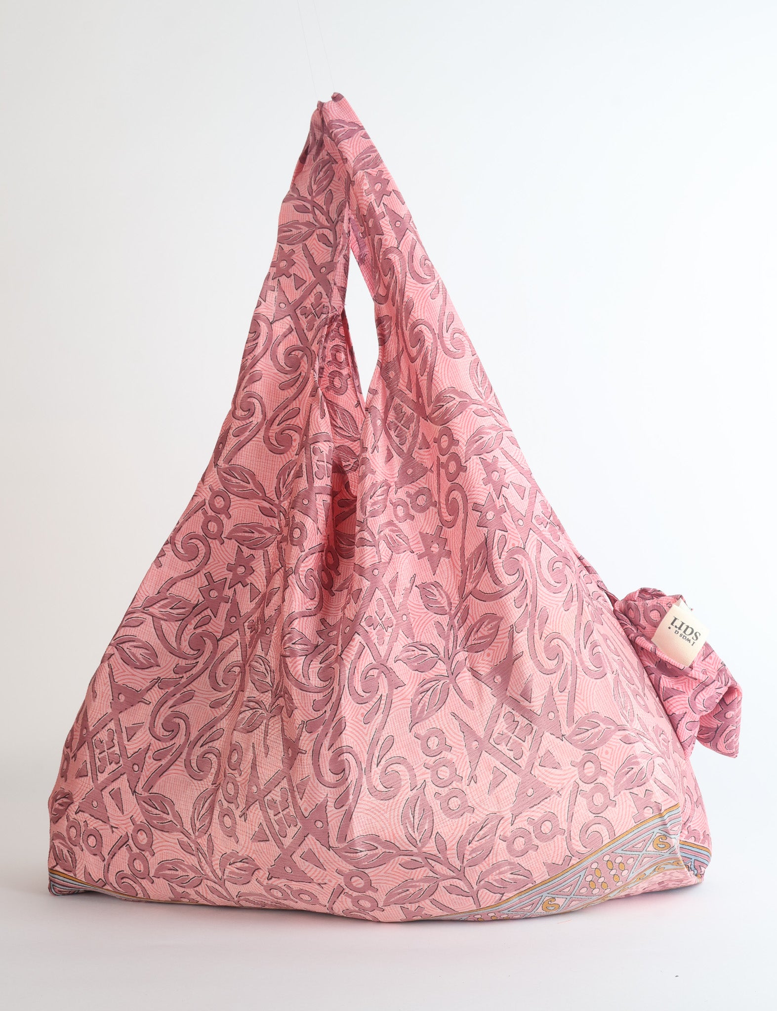 Pink reusable bag with abstract floral and geometric pattern, hanging with visible fabric texture and a small tag on the side