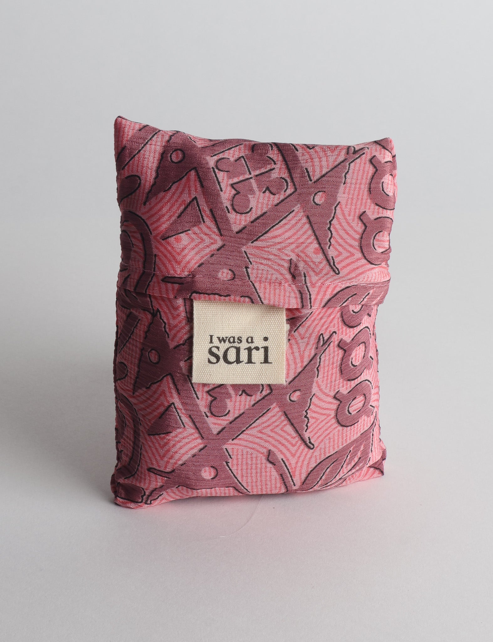 Pink reusable bag with abstract dark pink and black pattern, folded with a beige label reading "I was a sari" visible