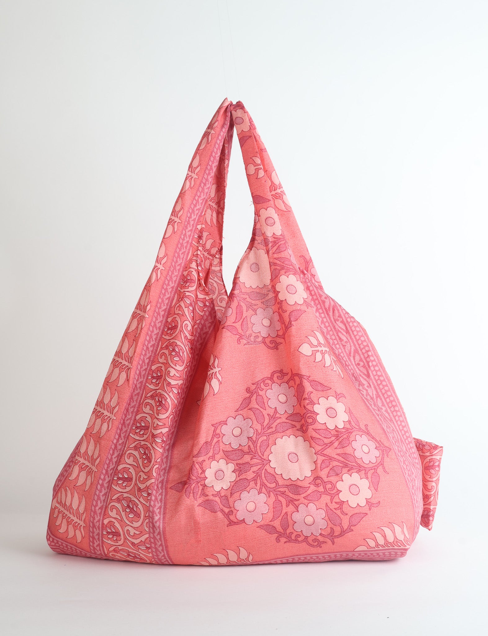 Pink reusable bag with paisley and floral patterns, shown hanging with handles together against a white background