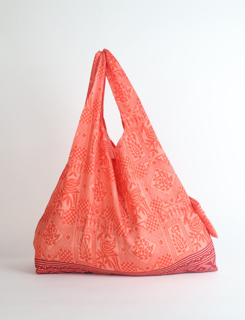Orange reusable bag with botanical and geometric patterns, flat base, and gathered handles, shown hanging against white background