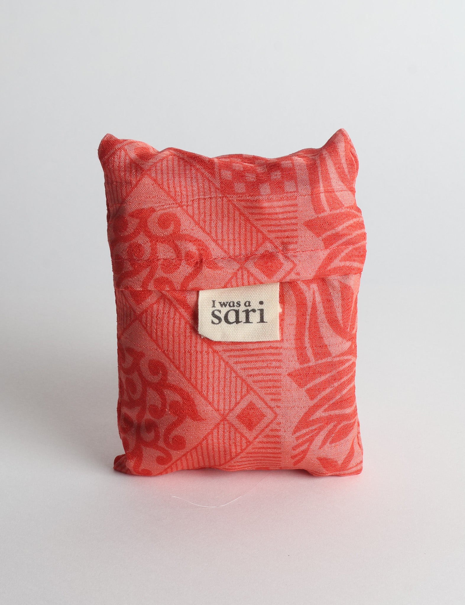 Orange reusable bag with botanical pattern and sewn label reading "I was a sari" shown folded against white background