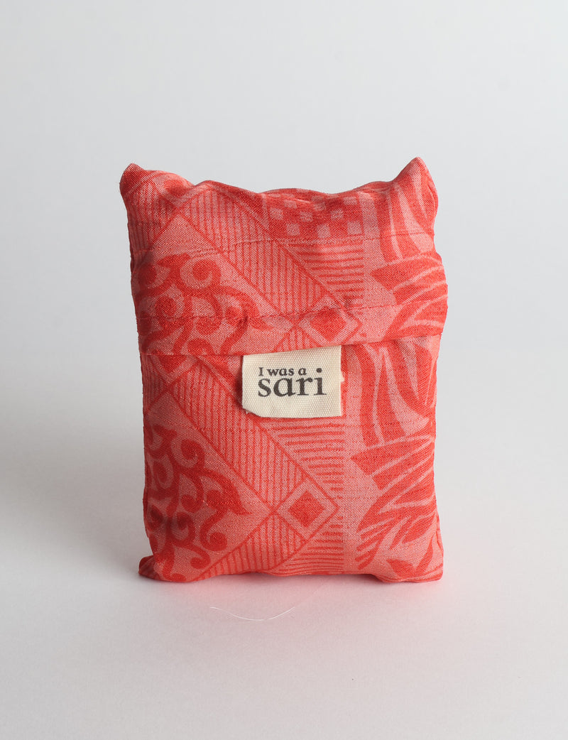 Orange reusable bag with botanical pattern and sewn label reading "I was a sari" shown folded against white background