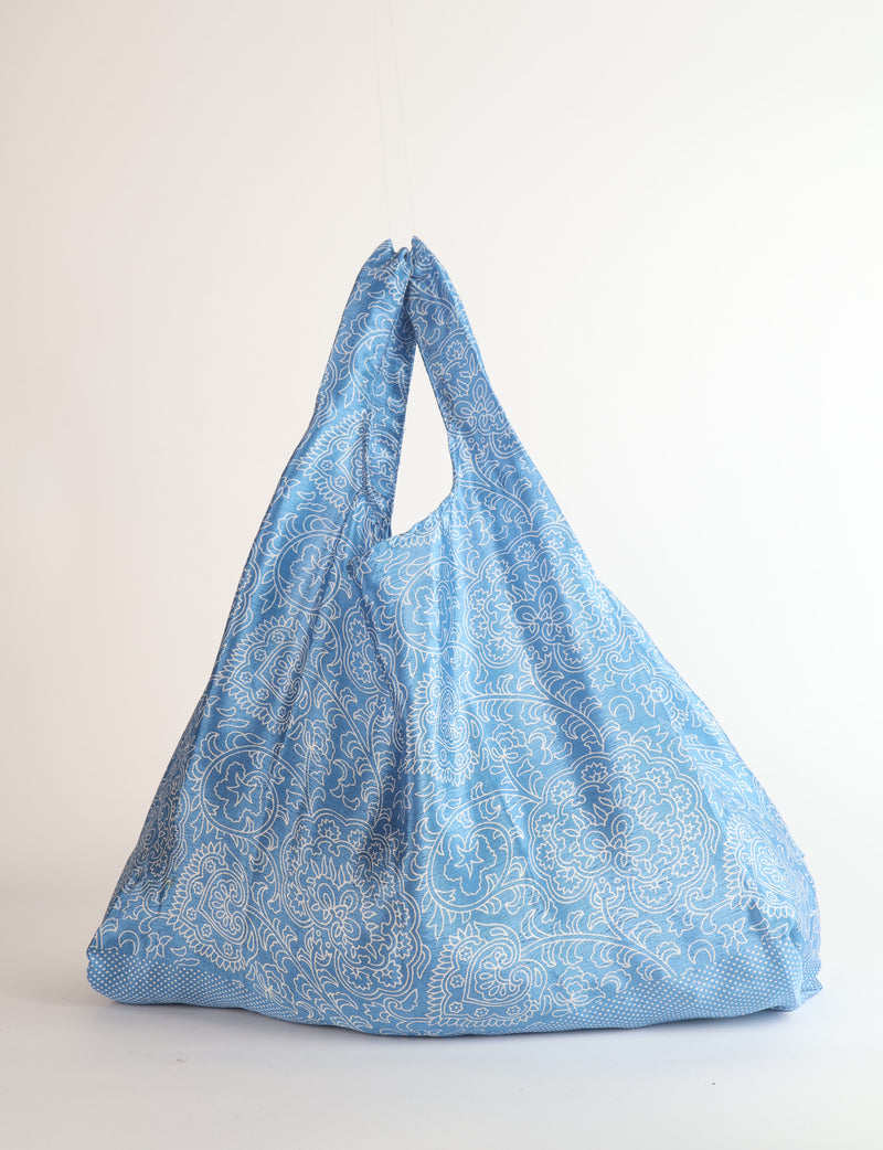 Blue reusable bag with white tropical paisley pattern, shown hanging with gathered handles and flat base
