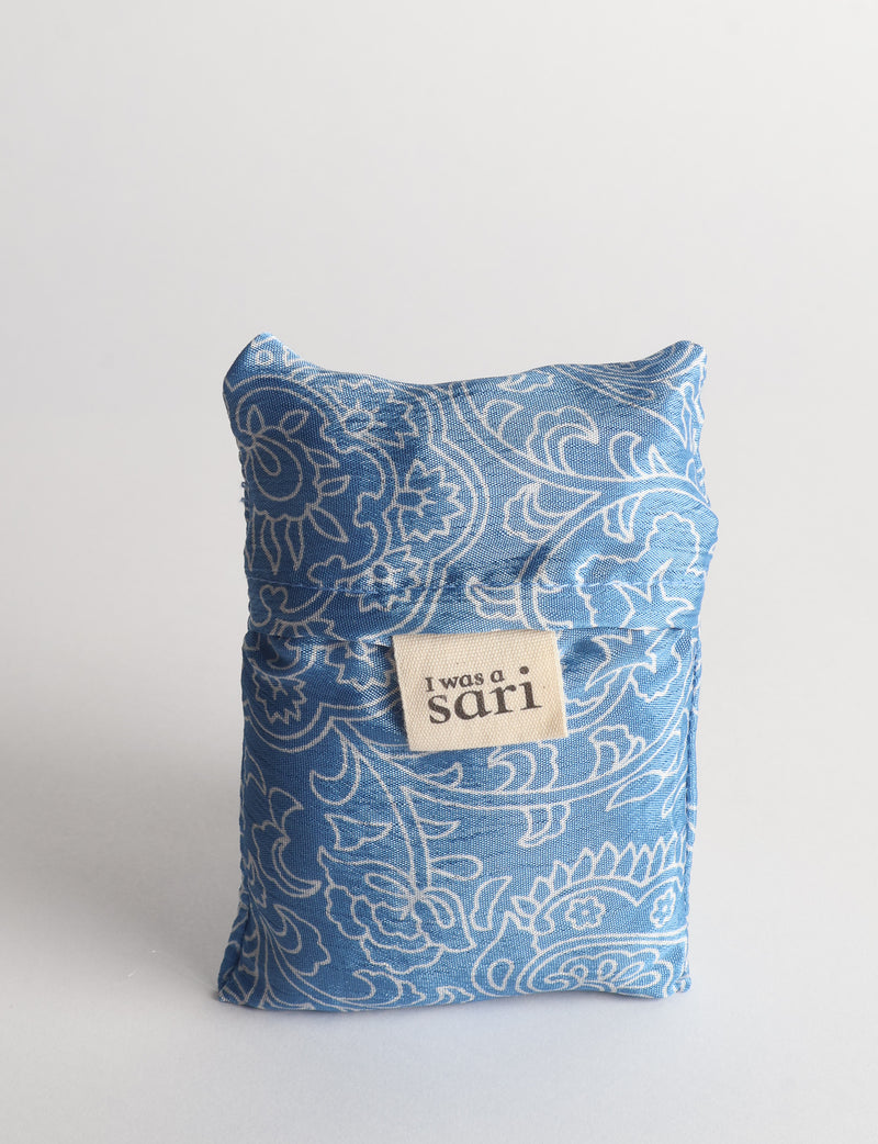 Blue reusable bag with white floral paisley pattern folded with a beige label reading "I was a sari" on front