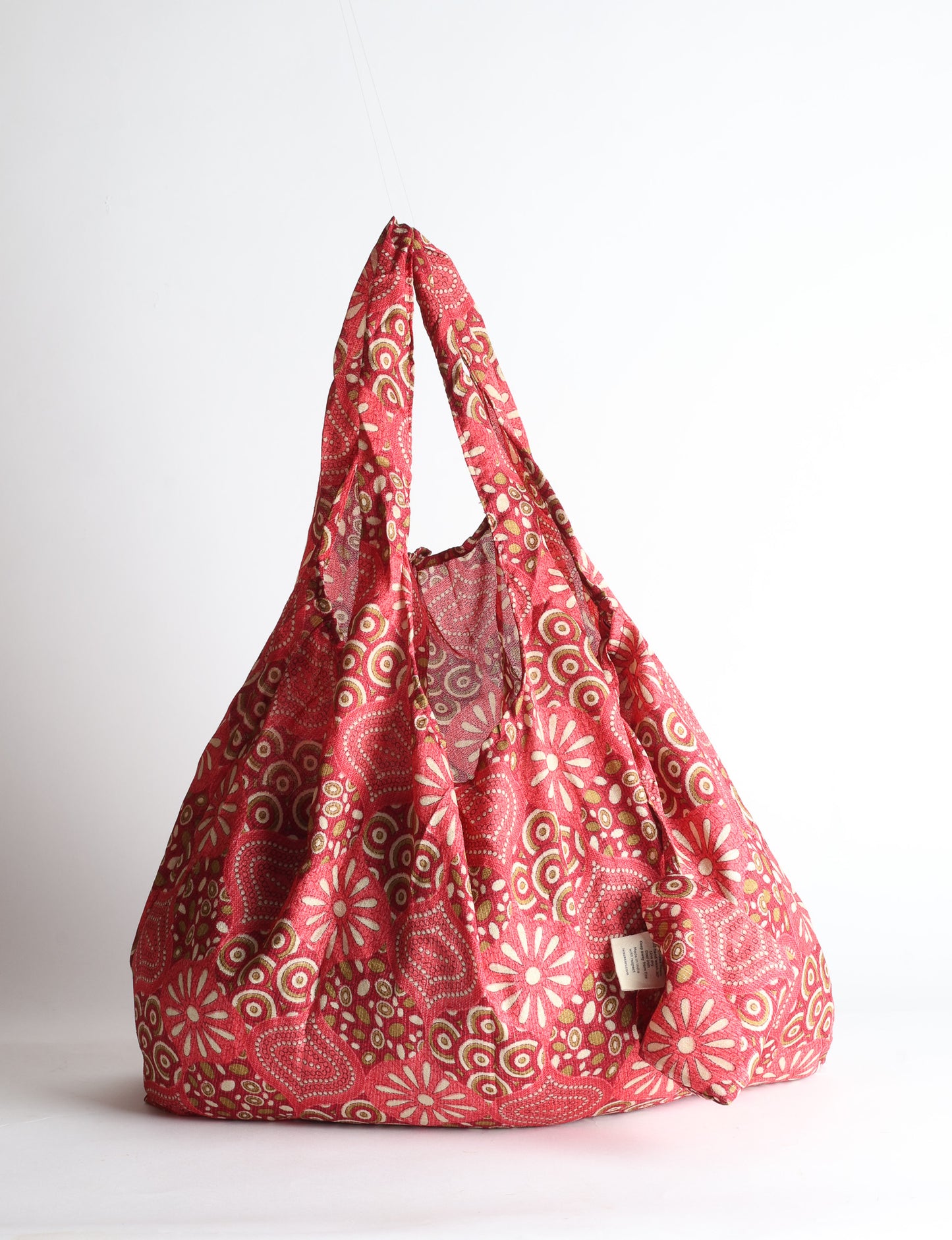 Blue reusable bag with tropical floral pattern in pink, yellow, and green, shown hanging with handles visible