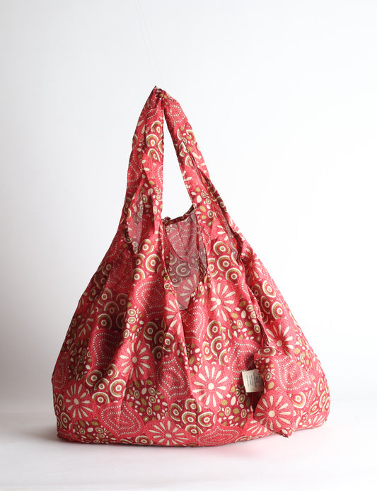 Blue reusable bag with tropical floral pattern in pink, yellow, and green, shown hanging with handles visible
