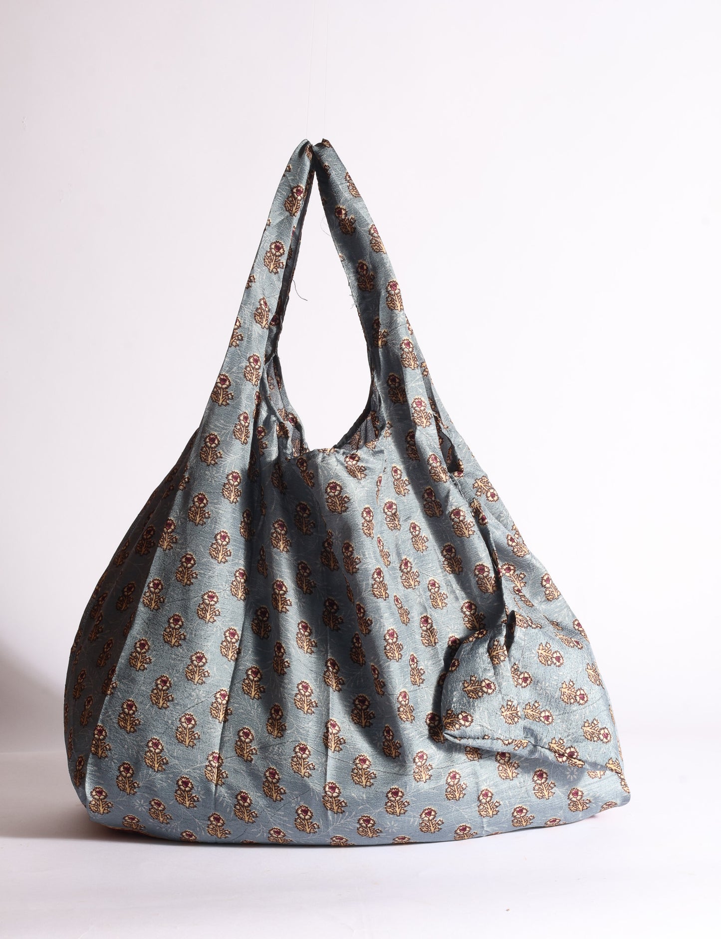 Blue reusable bag with tropical floral pattern in pink, yellow, and green, shown hanging with handles visible