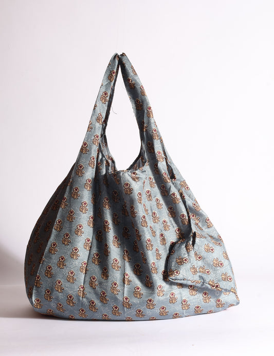 Blue reusable bag with tropical floral pattern in pink, yellow, and green, shown hanging with handles visible