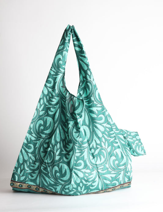Blue reusable bag with tropical floral pattern in pink, yellow, and green, shown hanging with handles visible