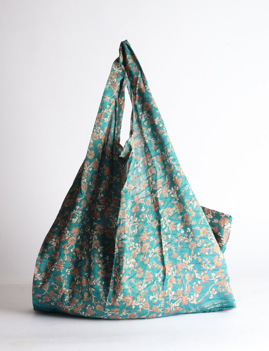 Blue reusable bag with tropical floral pattern in pink, yellow, and green, shown hanging with handles visible