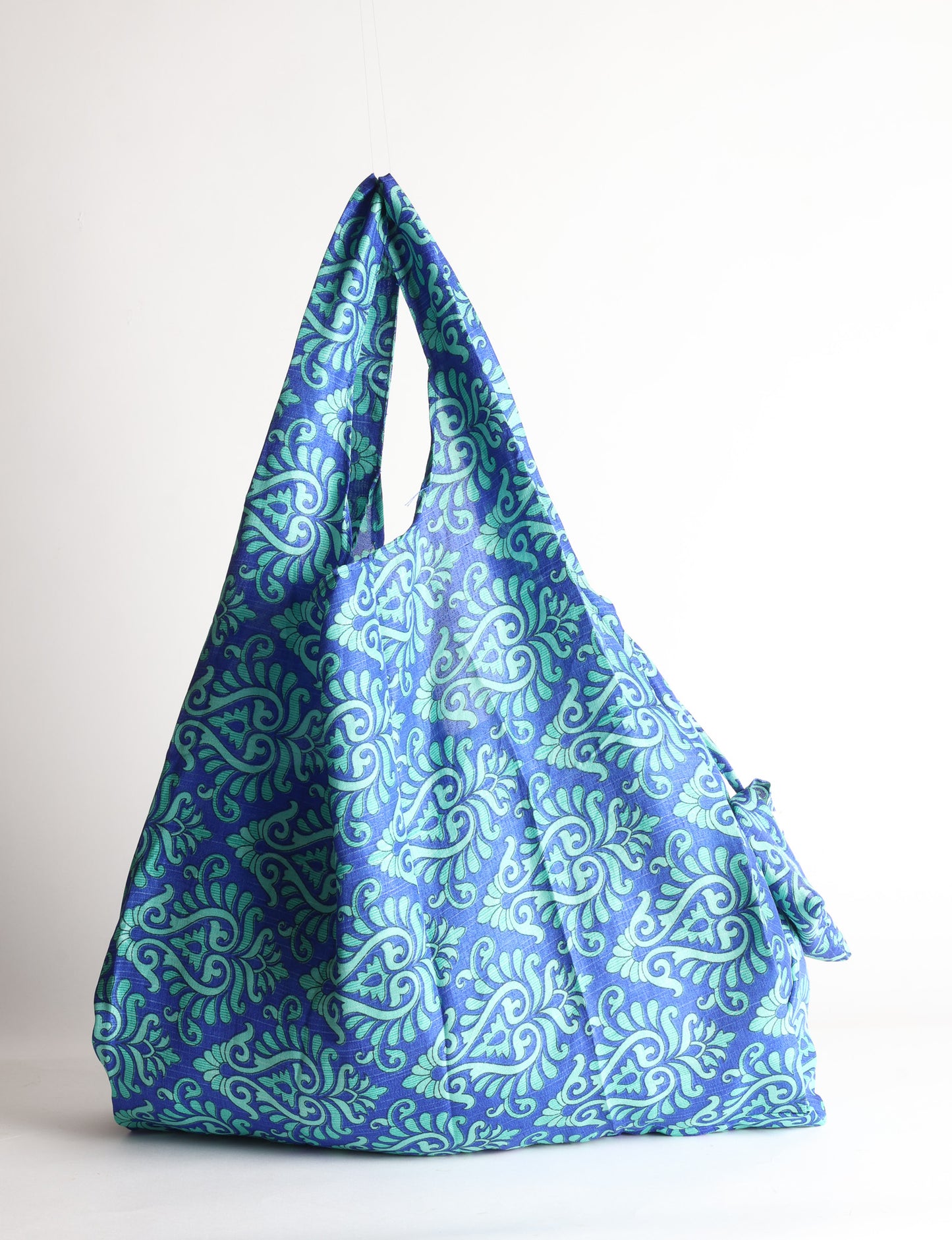 Blue reusable bag with tropical floral pattern in pink, yellow, and green, shown hanging with handles visible