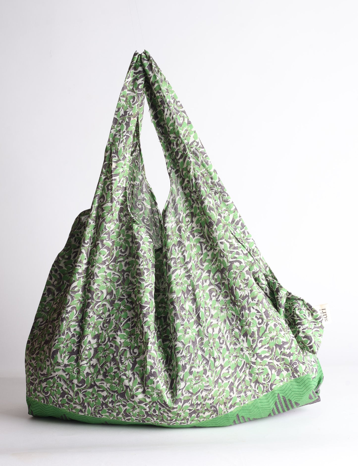 Blue reusable bag with tropical floral pattern in pink, yellow, and green, shown hanging with handles visible