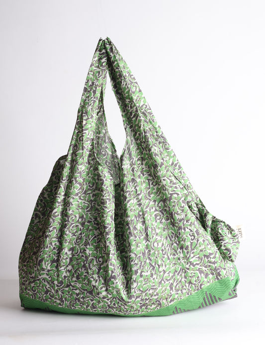 Blue reusable bag with tropical floral pattern in pink, yellow, and green, shown hanging with handles visible
