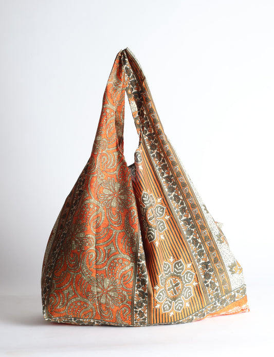 Blue reusable bag with tropical floral pattern in pink, yellow, and green, shown hanging with handles visible
