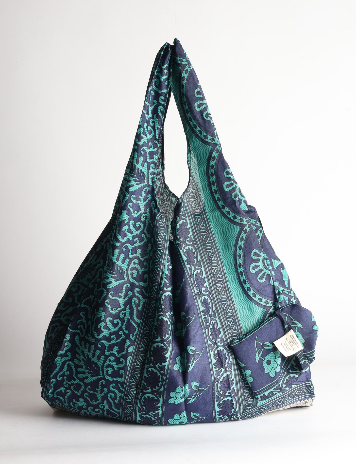 Blue reusable bag with tropical floral pattern in pink, yellow, and green, shown hanging with handles visible