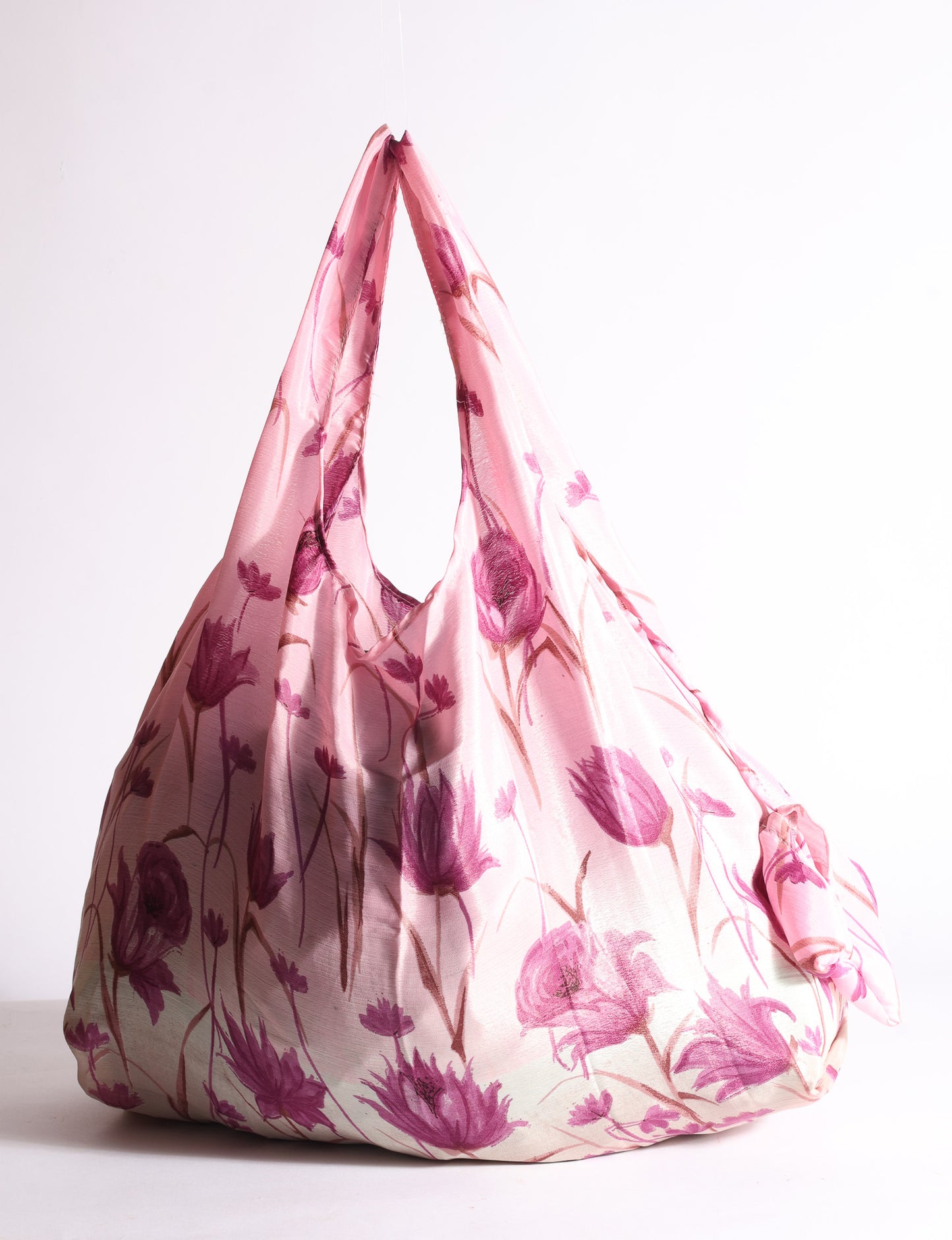 Blue reusable bag with tropical floral pattern in pink, yellow, and green, shown hanging with handles visible