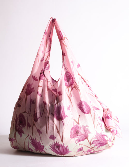 Blue reusable bag with tropical floral pattern in pink, yellow, and green, shown hanging with handles visible
