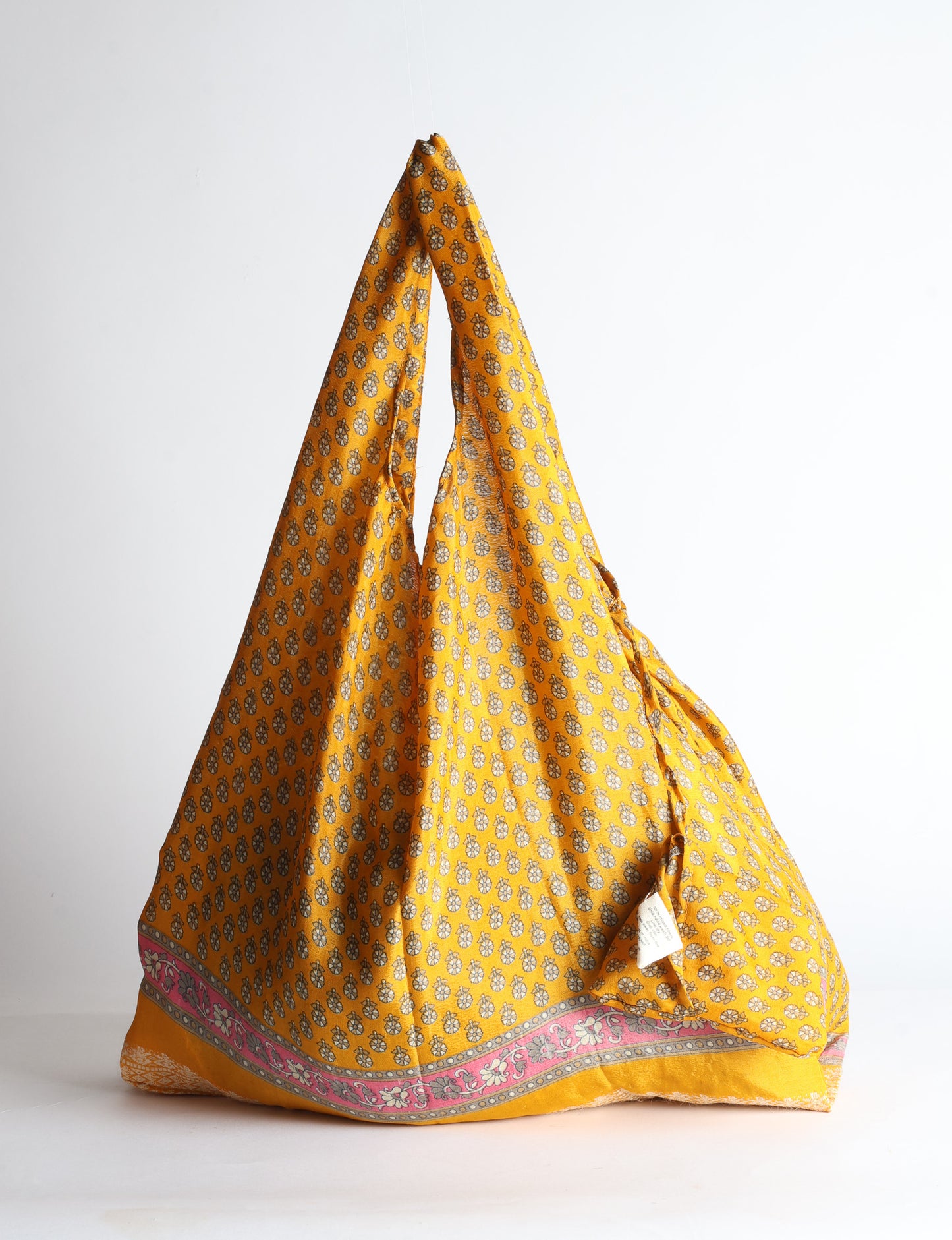 Blue reusable bag with tropical floral pattern in pink, yellow, and green, shown hanging with handles visible