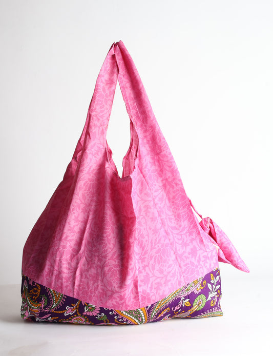 Blue reusable bag with tropical floral pattern in pink, yellow, and green, shown hanging with handles visible